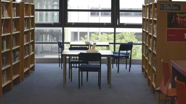 A library with a blue chair at a table. The chairs are empty. The tables are empty