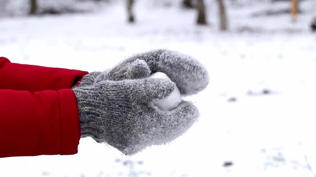 A man in gray knitted mittens makes a snowball in a snowy park.Winter enterainment,playing active games.