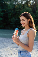 Healthy smiling woman holding reusable bottle with water infused with green mint and verbena leaves