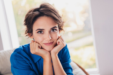 Photo of positive adorable sweet homey girl sitting with two hands under face day light indoors