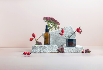 A dropper bottle with vitamin C and whey oil and a jar of hand or face cream on a podium made of stone and rosehip fruits. Anti-aging antioxidant cosmetic serum with vitamin C, natural cosmetics.