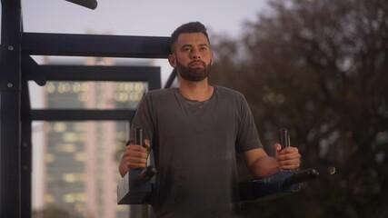Athletic man performing leg lift exercises in outdoor fitness equipment. Focused individual strengthening core muscles during evening workout at an urban park.