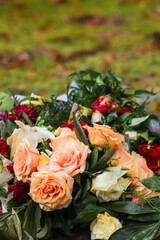 Funeral bouquets made of different colored roses in the cemetery's urn grove. Beautiful memorial flowers. Grave flowers after the rain. Empty space for text.