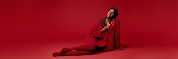 African American woman dressed in a red outfit sitting confidently on floor, wearing large stylish...