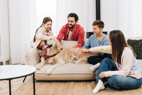 Happy family petting their golden retriever dog on sofa at home - Powered by Adobe