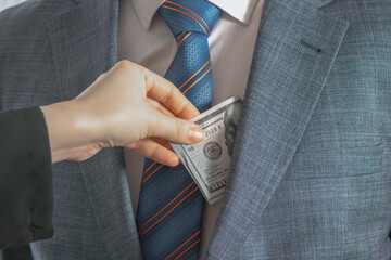 Dollar bills are dropped into the pocket of a man in a suit and tie. Give a bribe. Corruption