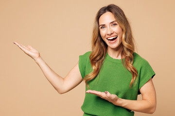Young smiling happy woman she wear green t-shirt casual clothes point hands arms aside indicate on...