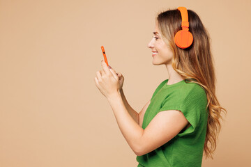 Side view young woman she wear green t-shirt casual clothes listen to music in headphones hold in...