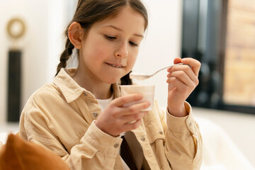 Girl enjoying yogurt at home: healthy eating habits for kids