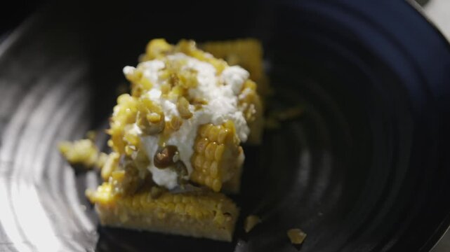 A plate of food with a yellowish color and a white sauce. The plate is black and the food is cut into small pieces