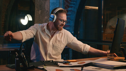 Happy funny positive businessman night office finish work fun fooling turning around on chair dancing listen to music in headphones dance enjoy song audio late time Caucasian business man guy male