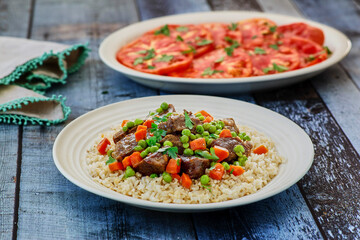 beef stew and gravy on a bed of rice served with a tomato salad on the side