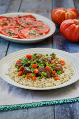 beef stew and gravy on a bed of rice served with a tomato salad on the side