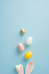 A vertical top view of colorful Easter eggs and bunny ears arranged on a soft blue background showcasing festive Easter themes