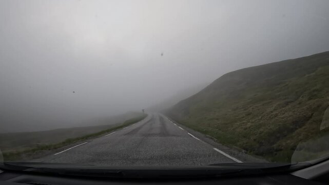 Driving on the E69 road through the tundra in northern Norway. Misty hills covered with grass and scattered stones surround the route, creating a remote and atmospheric landscape.