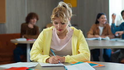 High school bullying upset stressed lonely Caucasian girl teen female woman schoolgirl student teenager writing task class desk university college children students mock bully throwing papers balls