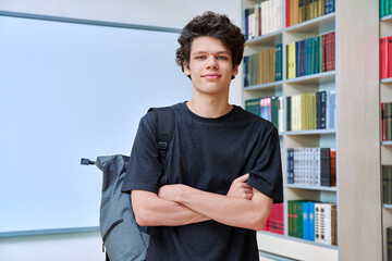 Portrait of college student guy with crossed arms inside library of educational building