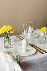 Happy Easter! Spring elegant table setting with white plates, egg cups, gold cutlery and vases with yellow flowers on a white tablecloth