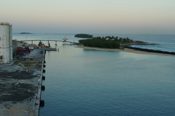 A pier equipped with fenders, industrial storage tanks, and piles of stones the port of Nassau in the Bahamas, one of the Caribbean islands, during sunrise.