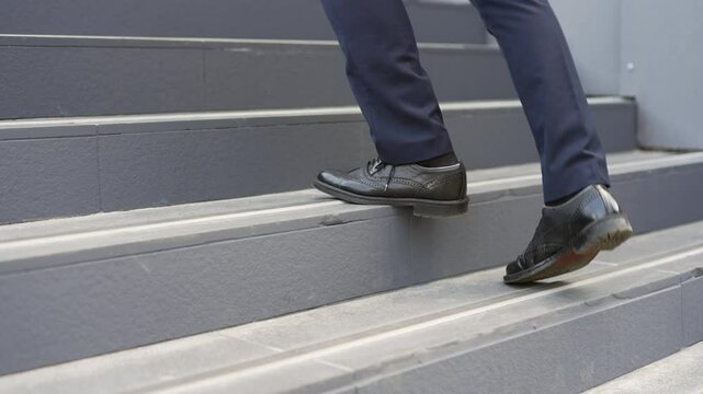 Close up of businessman's legs walking up stairs outside modern office building. Entrepreneur in formal suit going to work on city street. Business grow up, urban lifestyle concept. Side and back view