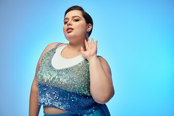 Young plus size woman poses confidently in vibrant blue sequined attire against soft backdrop