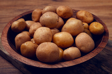 Freshly harvested small potatoes in a wooden bowl resting on a rustic surface ready for cooking or preparation for a meal