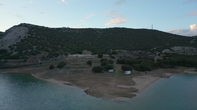 Camper vans parked on a wild spot in Lake Polyfyto drone aerial view at sunset in Greece