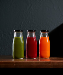 green red orange cold-pressed juice bottles on wooden table with dark background