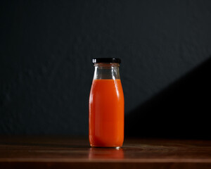 Orange Cold-pressed juice bottle on wooden table with dark background