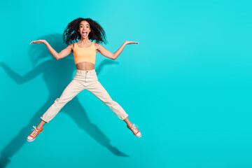 Obraz premium Energetic young woman jumping against a bright teal backdrop, exuding joy and confidence
