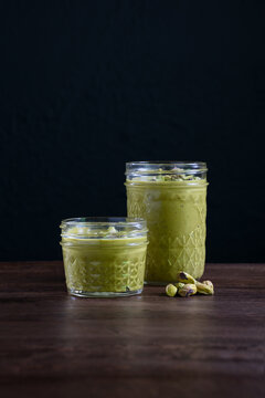 Pistacio Butter in glass jar with nuts on wooden table dark background