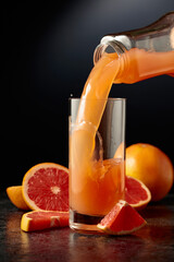 Grapefruit juice is poured from a bottle into a glass.