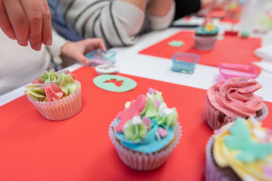 Young girl with mother decorating cupcakes during a baking class preparing muffins and cupcake for birthday party celebration