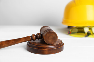 Accident at work concept. Gavel and construction worker's protective gear on white wooden table, selective focus