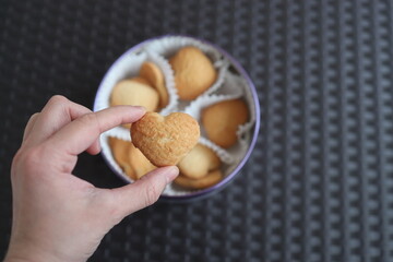 A set of sweet cookies in the shape of hearts as a gift for Valentine's Day. One cookie in hand.