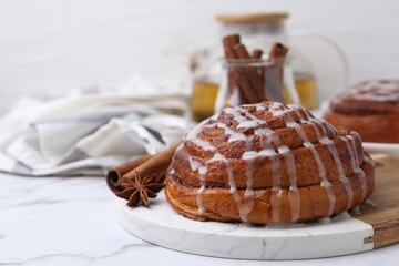 Tasty cinnamon roll with cream and spices on white marble table, closeup. Space for text