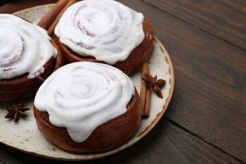 Tasty cinnamon rolls with cream and spices on wooden table, closeup