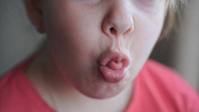 Girl moves lips and folds them into a tube. Tongue sticks out slightly. Close-up of mouth and playful expression. Funny moment, curious look. Macro shot with detailed texture. Soft natural lighting