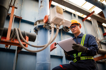 A male maintenance engineer is checking a pressure valve system in a water pipe and recording values