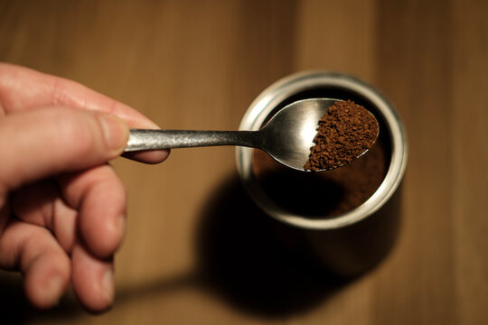 Hand holding teaspoon of instant coffee over container