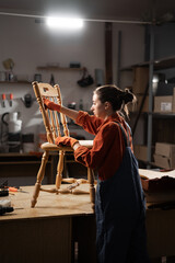 Start-up and small business concept. Young woman carpenter or handyman sanding a wooden chair doing restoration or repair of old wooden furniture