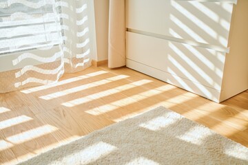 Warm morning sunlight casts striped shadows through sheer curtains onto a natural wooden floor. A...