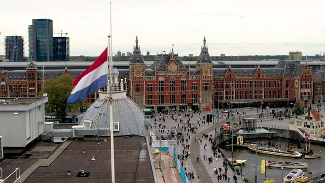 Beautiful aerial cinematic footage of Holland Flag and in the back the Amsterdam Centraal Train Station and its historic hub with canals, bikes, cafes. Netherlands