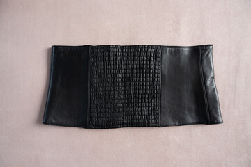 Black leather corset belt with textured panel on beige background