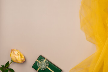 Gift box, rose with yellow tulle fabric texture on beige background. Flat lay, top view. Copy space