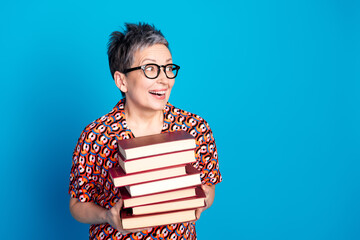 Smiling stylish senior woman holding a stack of books against a vibrant blue background
