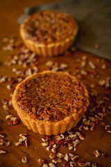 Tartaletas de nuez caramelizada sobre tabla de madera oscura con nueces picadas alrededor