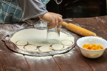 A woman's hand makes round blanks from dough on a wooden table