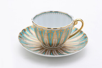 Elegant porcelain teacup sitting on matching saucer, decorated with gold and turquoise patterns