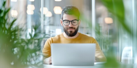 business startup with expansion. A man works on a laptop surrounded by plants in a bright, modern workspace.